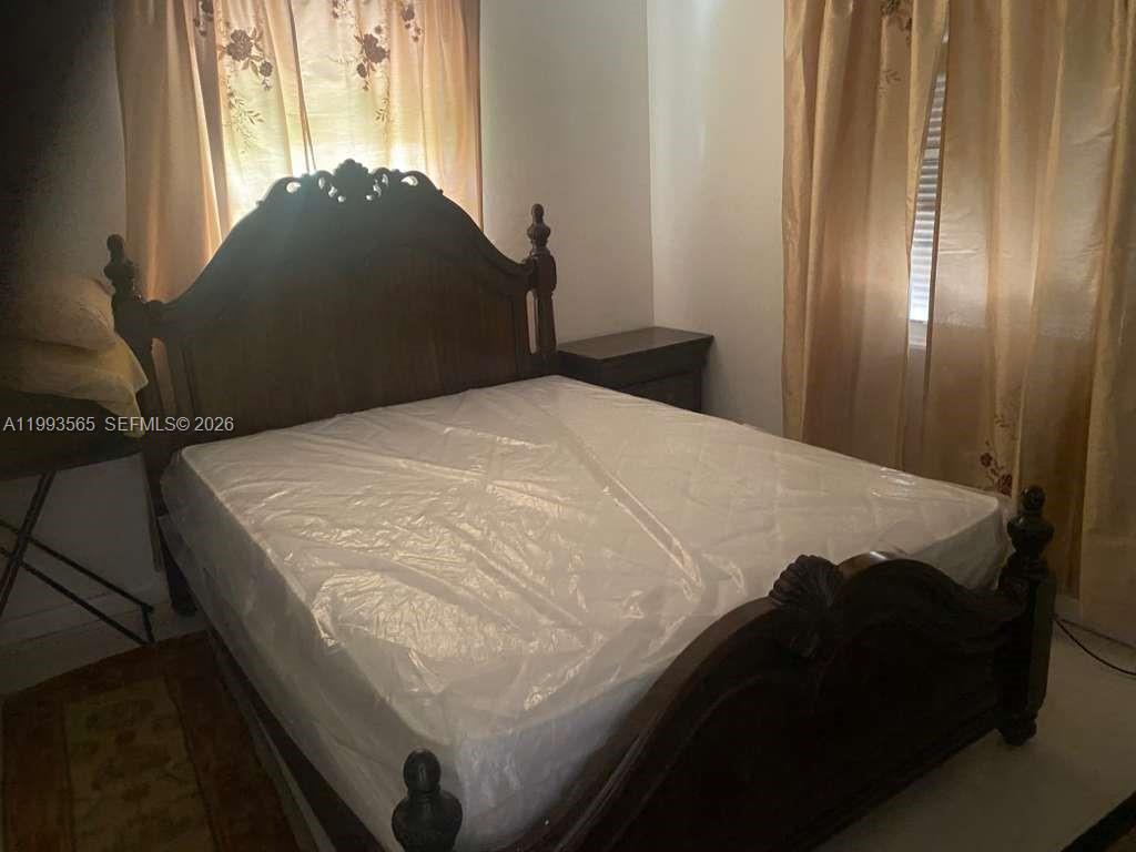 A bedroom features a dark wood bed frame with a mattress and gold curtains — 712 57th St, West Palm Beach FL 33407, WEST PALM BEACH, FL