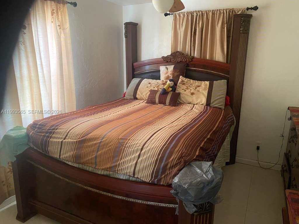 A bedroom features a large wooden bed frame with a striped comforter and curtains — 712 57th St, West Palm Beach FL 33407, WEST PALM BEACH, FL