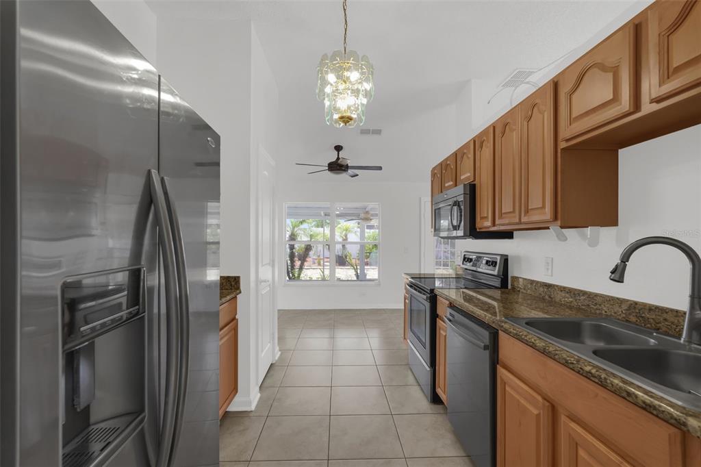 A kitchen with wood cabinets, granite countertops, stainless steel appliances, and tile flooring — 1747 POMPANO DRIVE, KISSIMMEE, FL