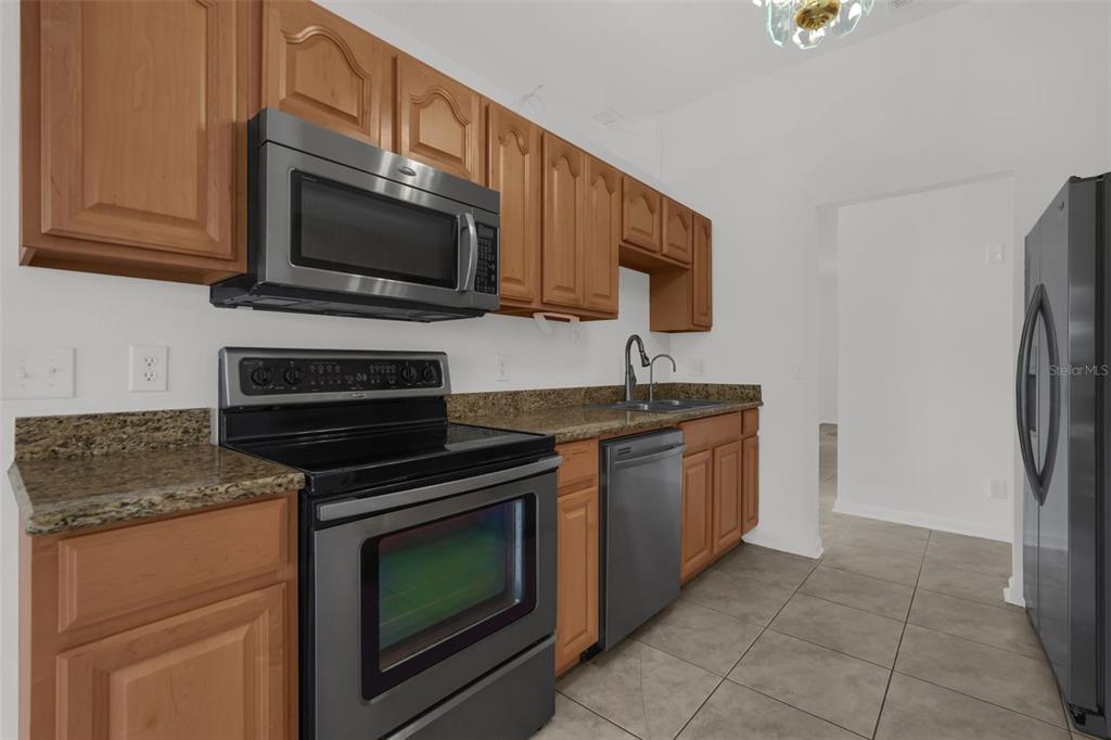 A kitchen features wood cabinets, granite countertops, stainless steel appliances, and tile flooring — 1747 POMPANO DRIVE, KISSIMMEE, FL