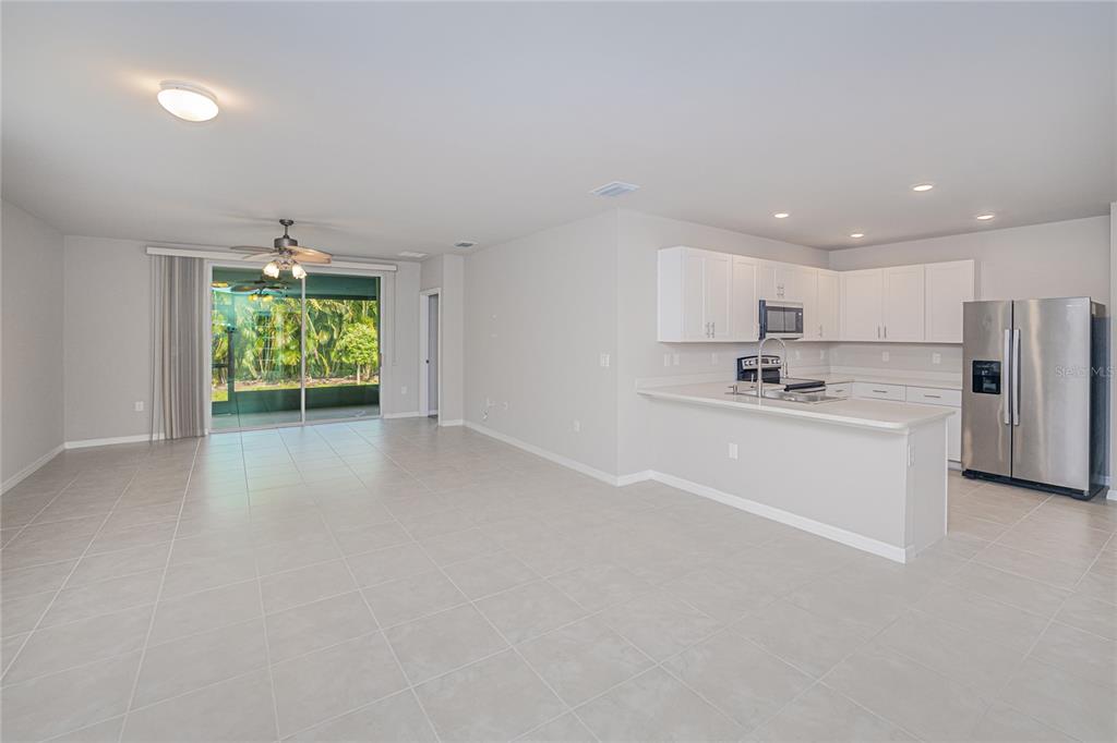 An open-concept kitchen and living area features light tile flooring, white cabinetry, and sliding glass doors — 7097 W LENOX CIRCLE, PUNTA GORDA, FL