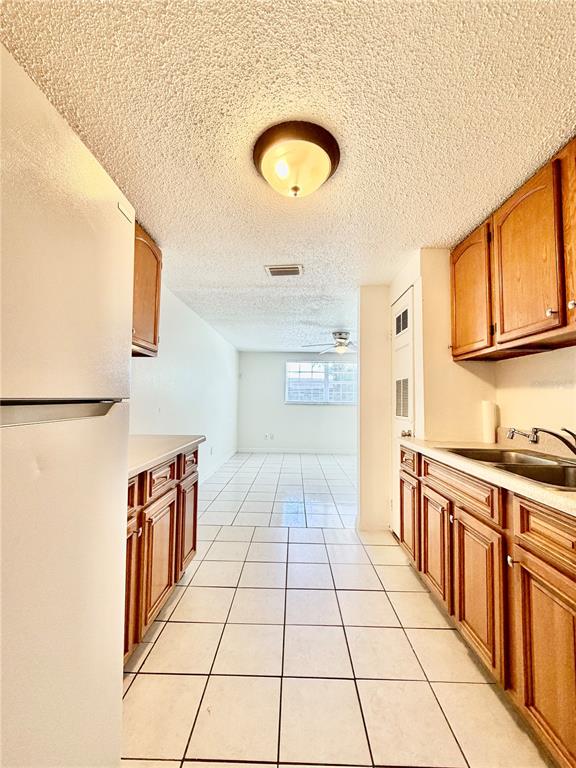 A galley kitchen with wood cabinets, white appliances, and tile flooring leads to a living area — 2204 IRENE STREET UNIT B, LUTZ, FL