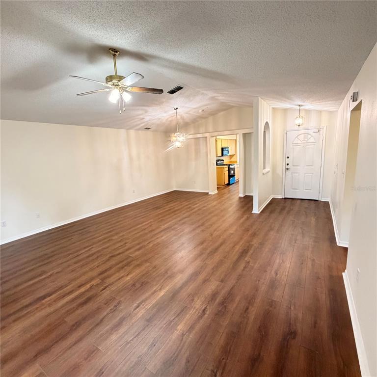 An open living area features wood-look flooring, a ceiling fan, and a view into the kitchen — 1025 MALLETWOOD DRIVE, BRANDON, FL