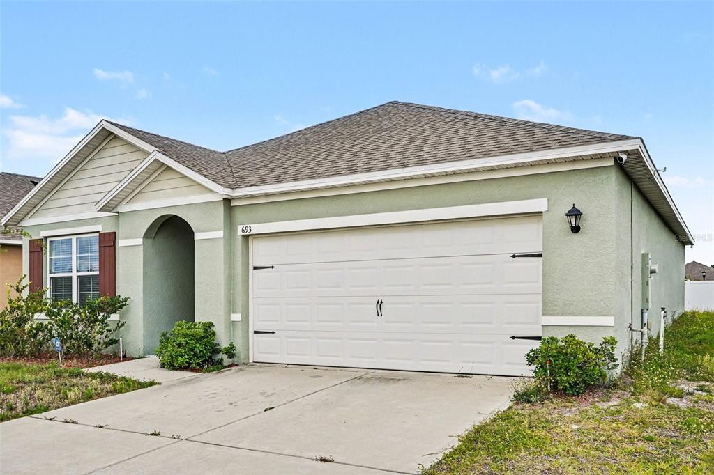 A single-story house with a light green stucco exterior and a two-car garage — 693 SQUIRES GROVE DRIVE, WINTER HAVEN, FL