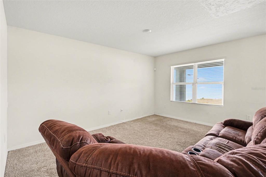A carpeted living room features a brown reclining sofa and a window with blinds — 693 SQUIRES GROVE DRIVE, WINTER HAVEN, FL