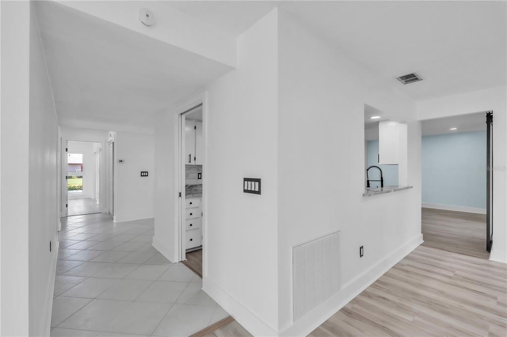 A hallway with tile flooring leads to a kitchen pass-through and adjacent living area — 6522 11TH AVENUE W, BRADENTON, FL