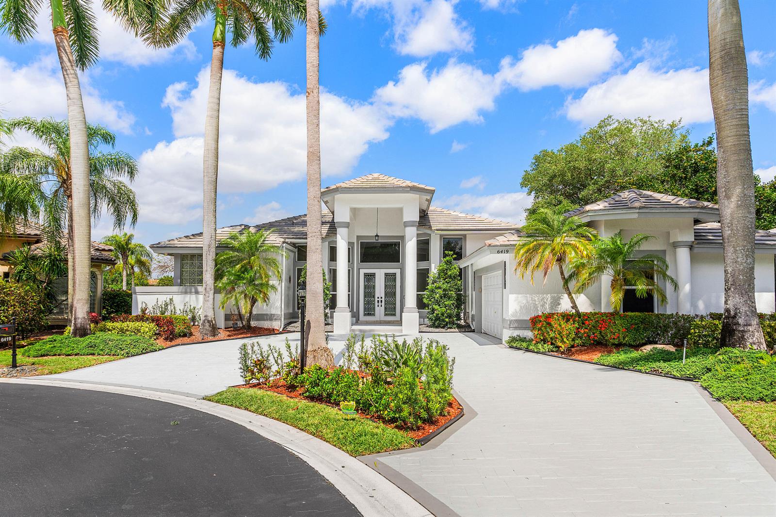 A single-story house with a paved driveway, palm trees, and a central entryway at dusk — 6419 NW 99th Drive, Parkland FL 33076, PARKLAND, FL