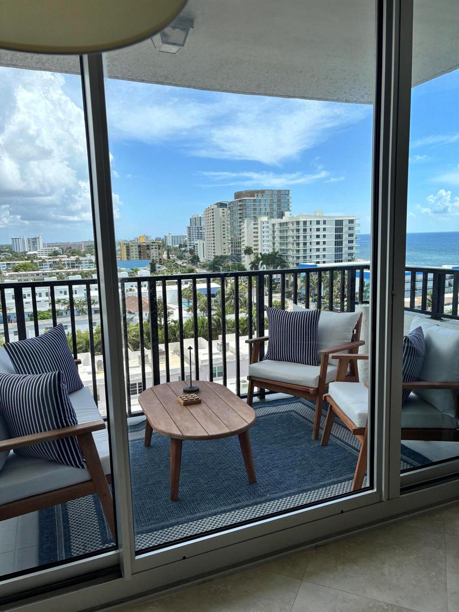 A balcony with wooden chairs, a coffee table, and a blue rug overlooks the ocean — 531 N Ocean Boulevard # 1107, Pompano Beach FL 33062, POMPANO BEACH, FL