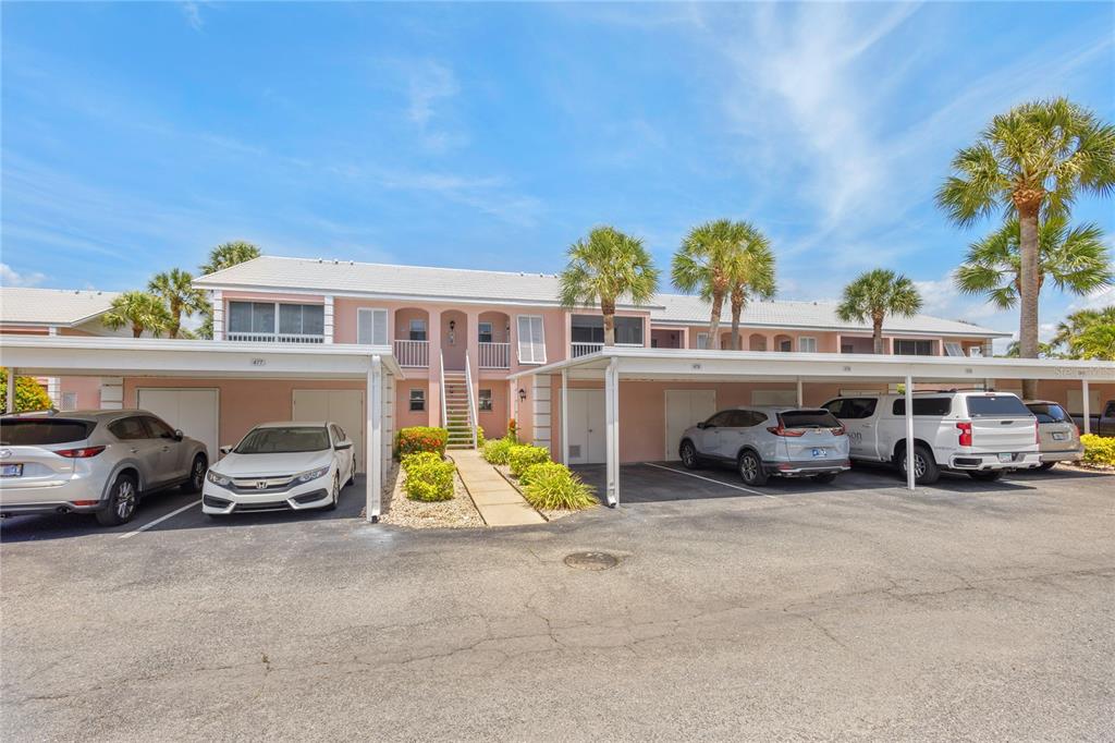 A covered carport area with parking spaces and storage units in front of a building — 436 CERROMAR LANE UNIT 478, VENICE, FL
