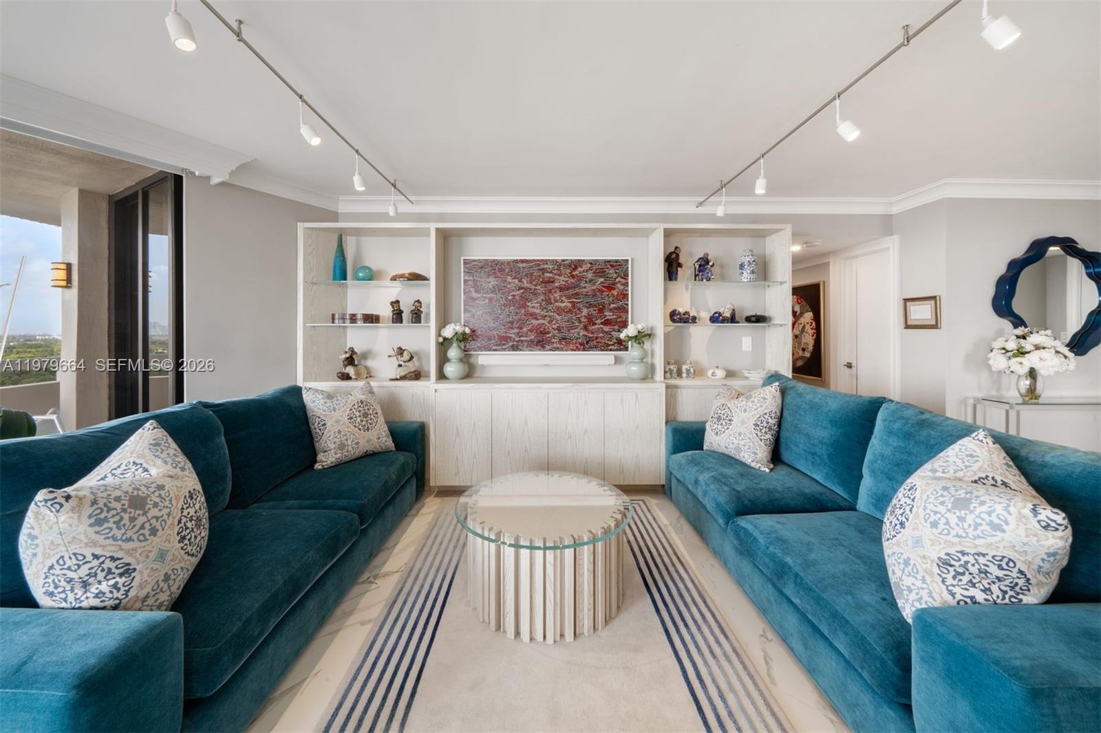 A living room features two teal sofas, a glass-topped coffee table, and built-in shelving units — 2000 Towerside Ter, Miami FL 33138, MIAMI, FL