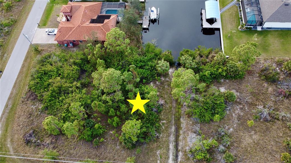 An aerial view shows a vacant, tree-covered residential lot adjacent to a canal and houses — 10281 ST PAUL DRIVE, PORT CHARLOTTE, FL