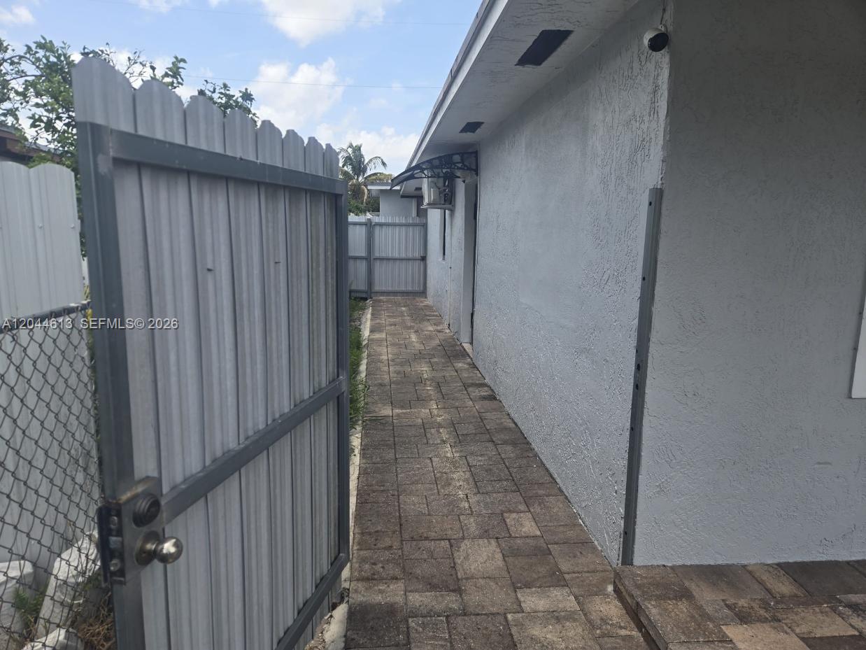 A paved walkway runs alongside the side of a gray house behind a metal gate — 735 SULTAN AVE # 1, Opa-Locka FL 33054, OPA-LOCKA, FL