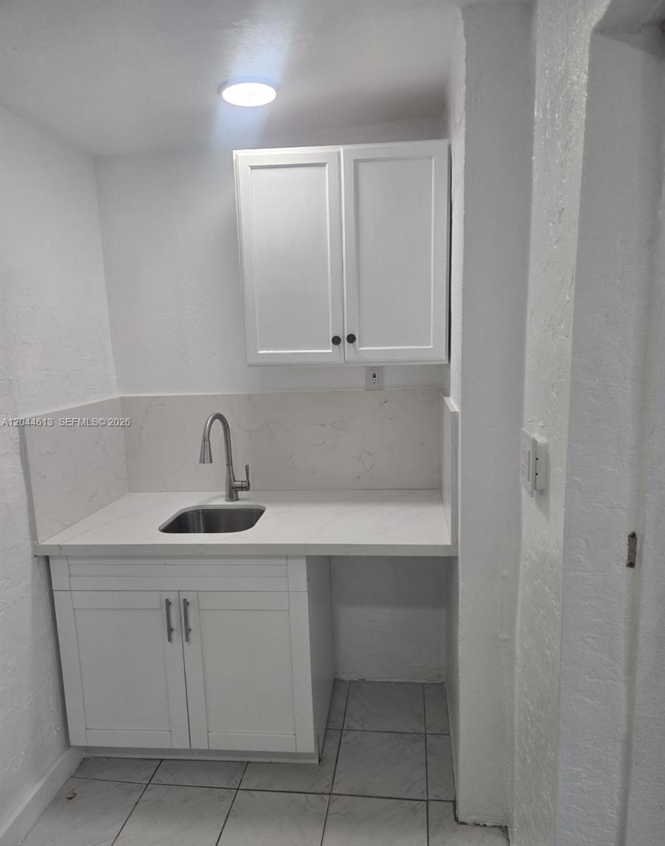 A small kitchenette features white cabinets, a stainless steel sink, and a marble-patterned backsplash — 735 SULTAN AVE # 1, Opa-Locka FL 33054, OPA-LOCKA, FL
