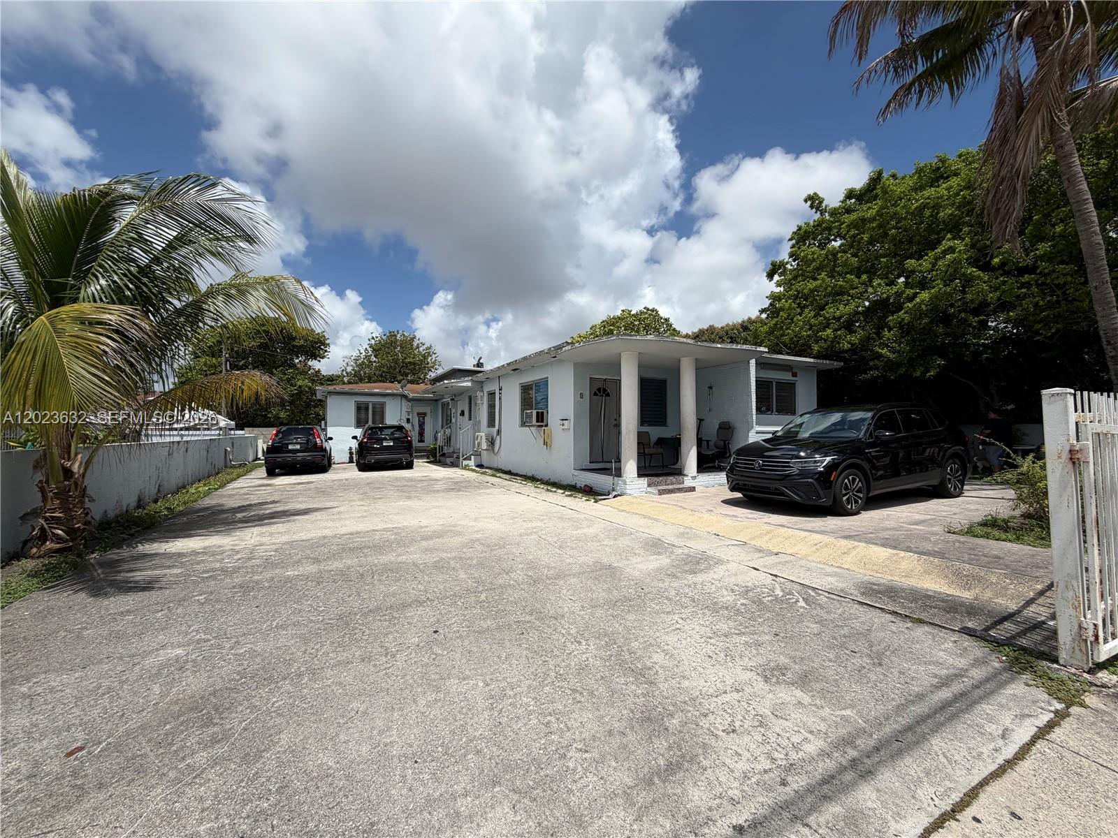 A light-colored single-story house features a concrete driveway with three parked cars and palm trees — 130 NW 16th Ave, Miami FL 33125, MIAMI, FL