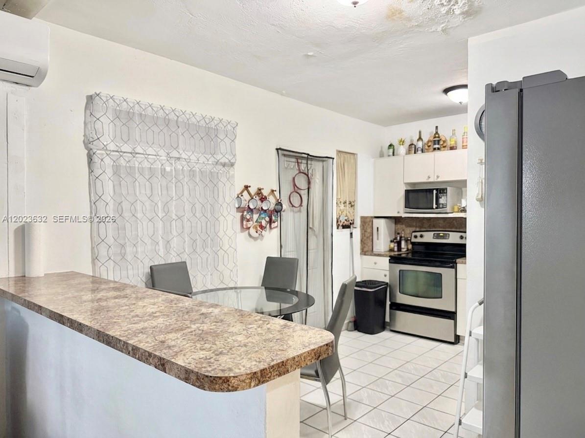 A kitchen and dining area features a breakfast bar, tile flooring, and white cabinetry — 130 NW 16th Ave, Miami FL 33125, MIAMI, FL