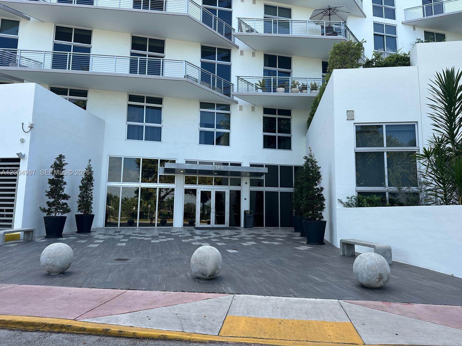 The exterior of a white multi-story building features a glass entrance and stone sphere bollards — 2001 Meridian Ave # 426, Miami Beach FL 33139, MIAMI BEACH, FL