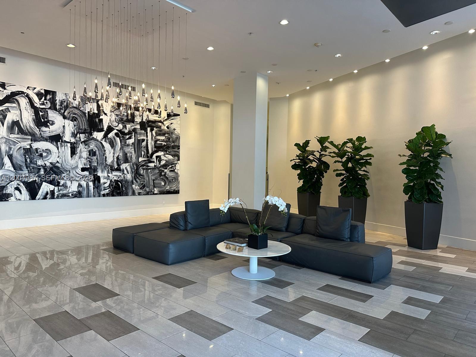 A modern lobby features a large abstract painting, a dark sectional sofa, and potted plants — 2001 Meridian Ave # 426, Miami Beach FL 33139, MIAMI BEACH, FL