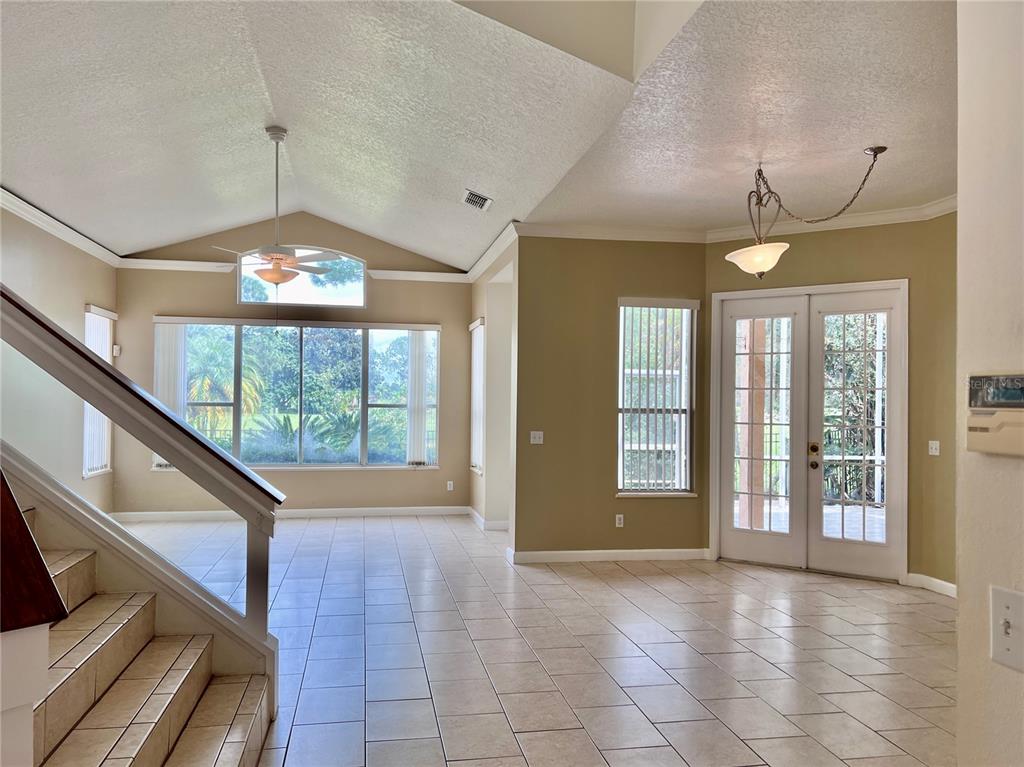 A bright living area with vaulted ceilings, tile floors, a staircase, and glass patio doors — 14300 DULCIMER COURT, ORLANDO, FL