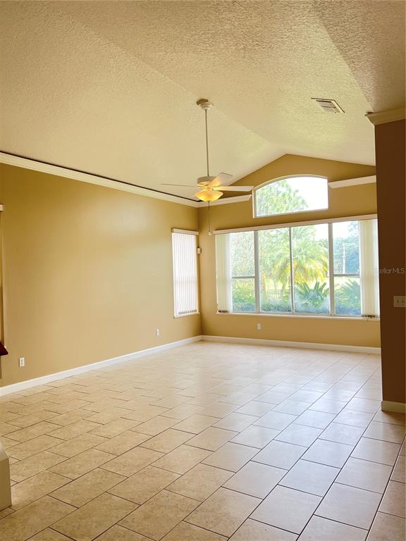 A spacious living room with vaulted ceilings, tile flooring, and large windows overlooking a yard — 14300 DULCIMER COURT, ORLANDO, FL