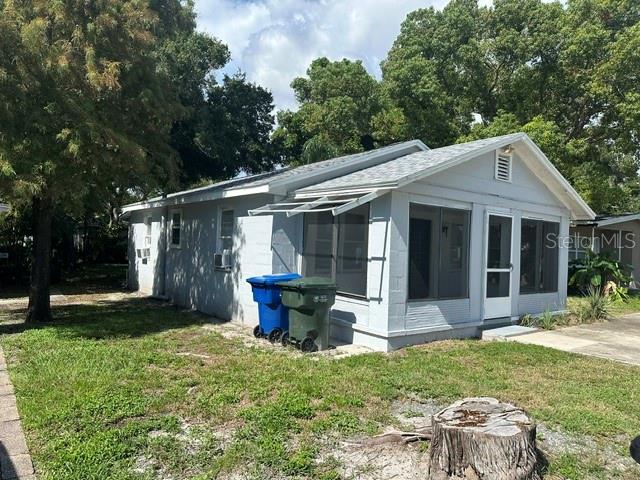 A light gray single-story house features a screened-in porch and two trash bins outside — 1010 ROSERY ROAD NW, LARGO, FL