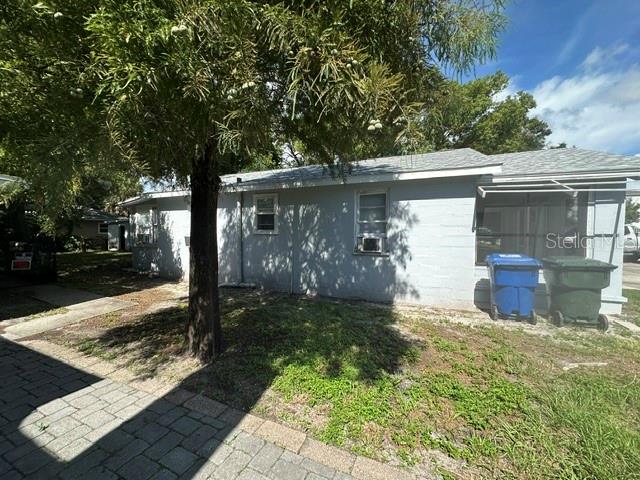 The exterior of a light gray, single-story house features a tree and two trash bins — 1010 ROSERY ROAD NW, LARGO, FL