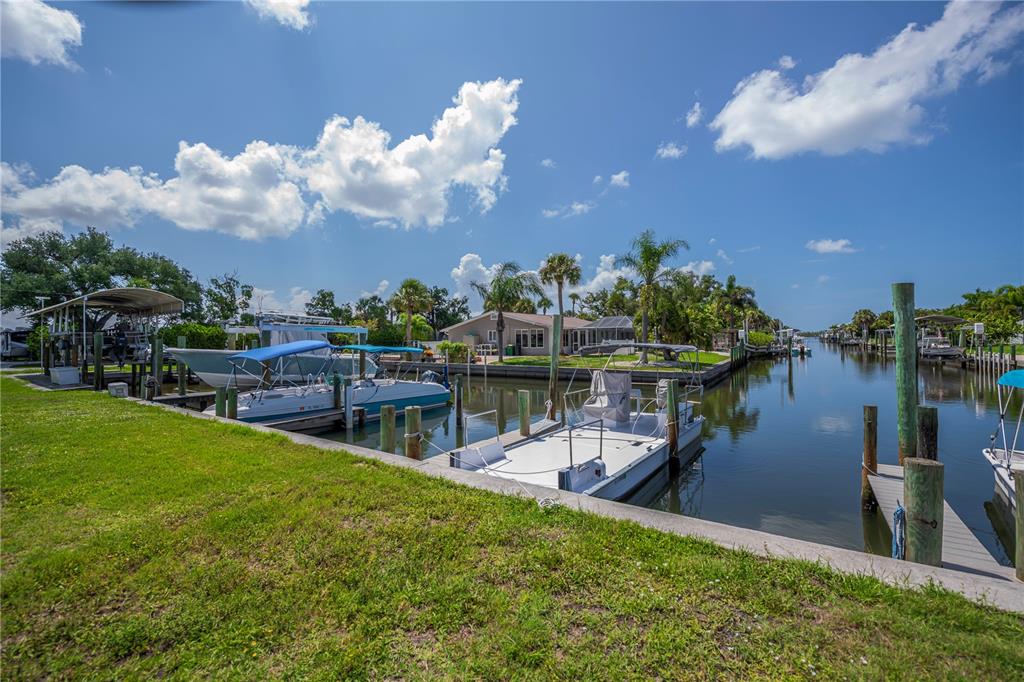 A canal view featuring several docked boats, wooden pilings, and a house in the background — 8152 SEASHELL STREET, ENGLEWOOD, FL