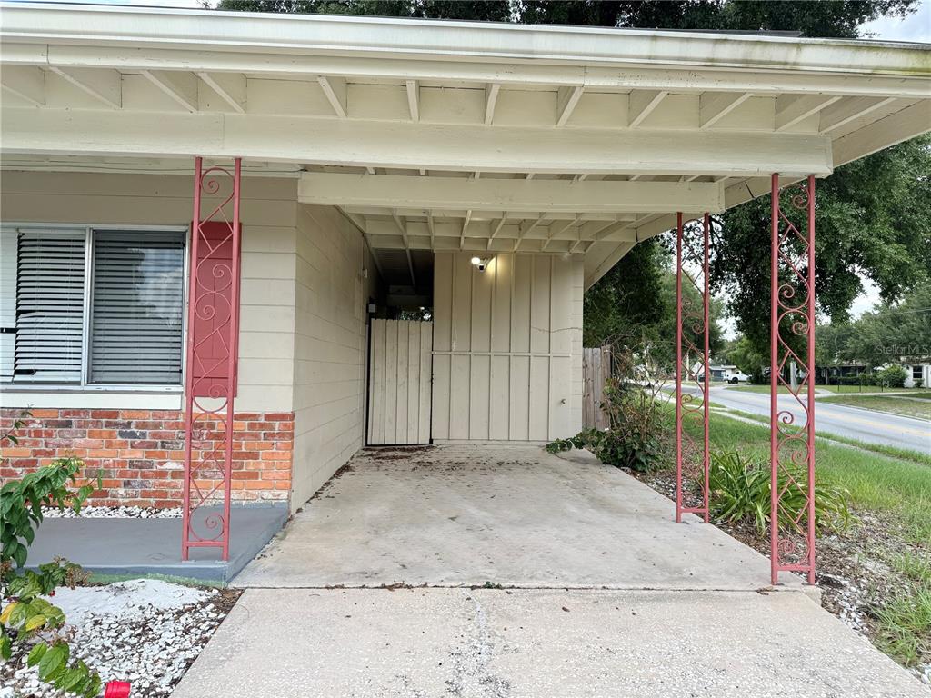 A concrete carport with decorative red metal posts sits beside a brick and siding house — 5801 JUDY DEE DRIVE, ORLANDO, FL