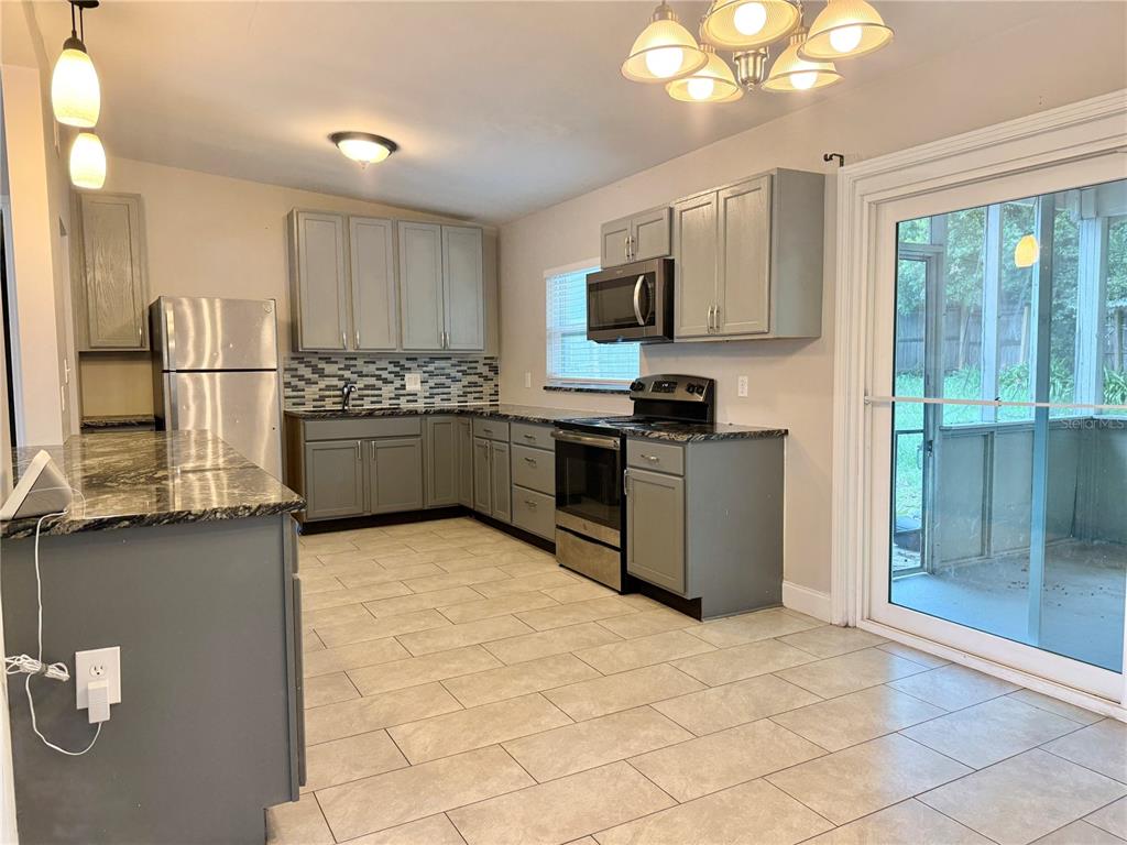 A kitchen features gray cabinets, granite countertops, stainless steel appliances, and light-colored tile flooring — 5801 JUDY DEE DRIVE, ORLANDO, FL
