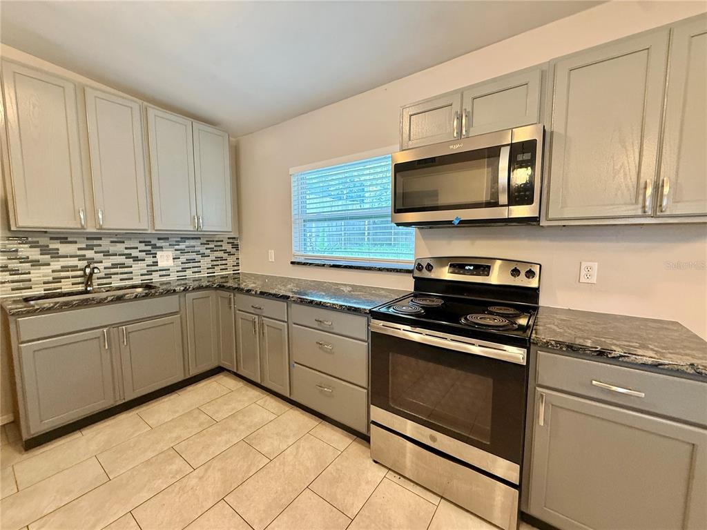 A kitchen features gray cabinets, stainless steel appliances, a tiled backsplash, and dark granite countertops — 5801 JUDY DEE DRIVE, ORLANDO, FL
