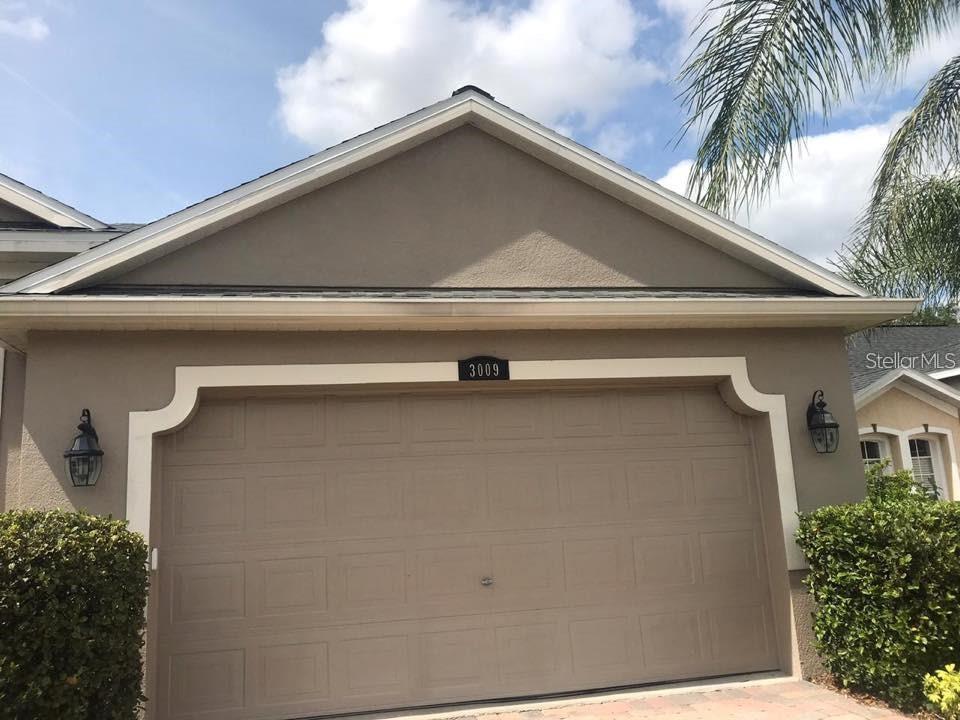 The exterior of a house features a tan stucco facade and a two-car garage — 3009 JUNEBERRY TERRACE, OVIEDO, FL