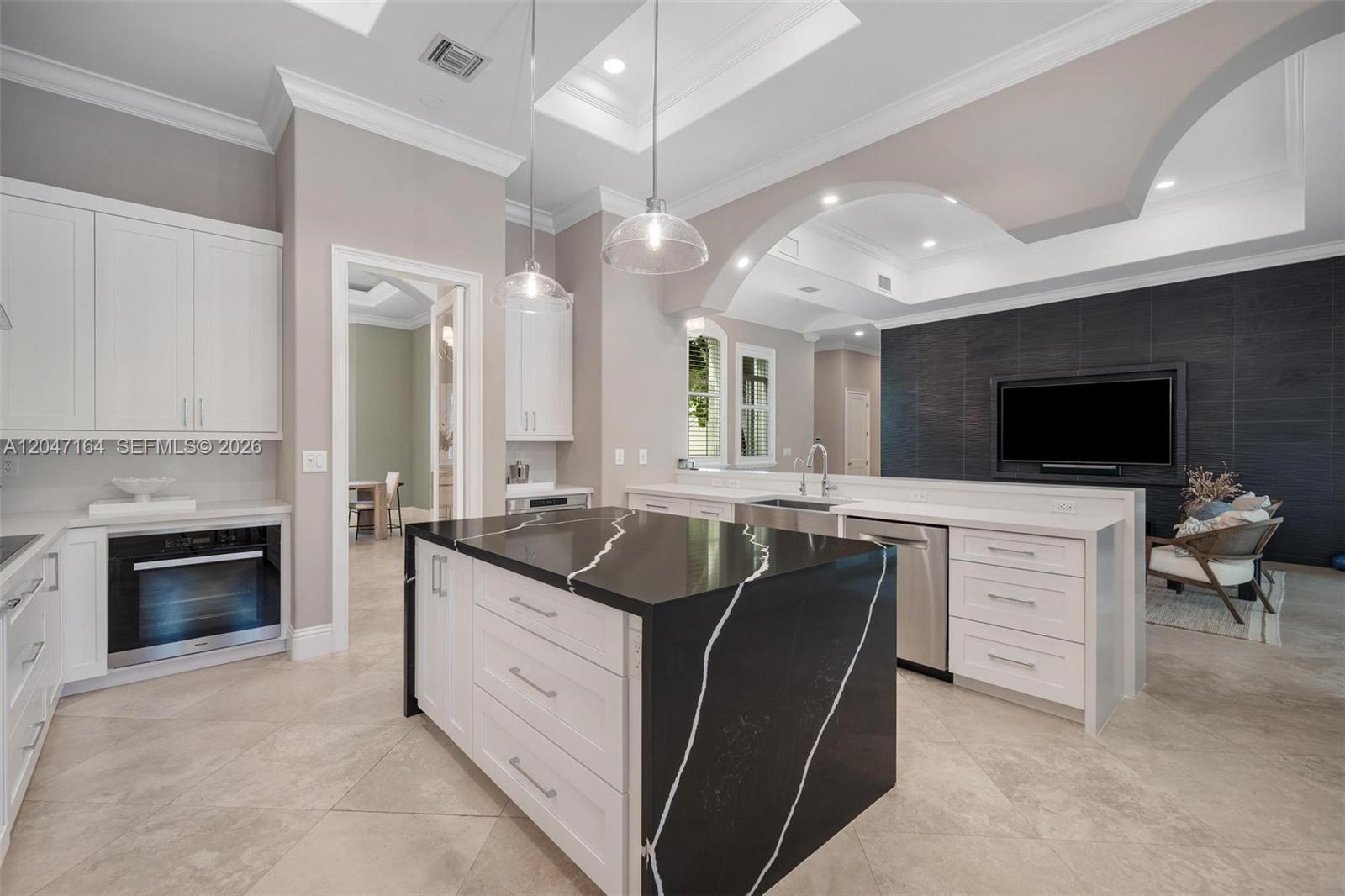 A modern kitchen features a black waterfall island, white cabinetry, and a dark accent wall — 6890 SW 94th St, Pinecrest FL 33156, PINECREST, FL