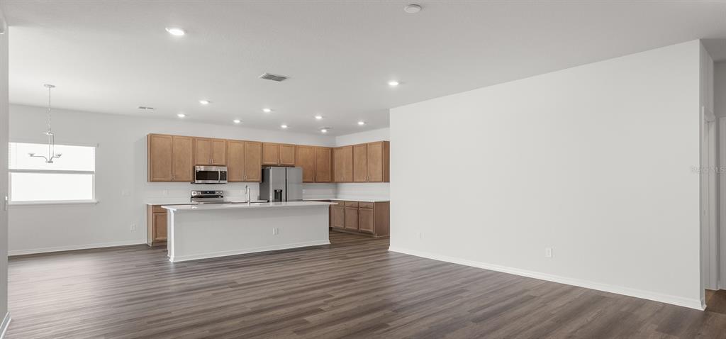 An open-concept kitchen features light wood cabinets, a central island, and dark wood-look flooring — 798 CYPRESS CREEK RUN, ST CLOUD, FL