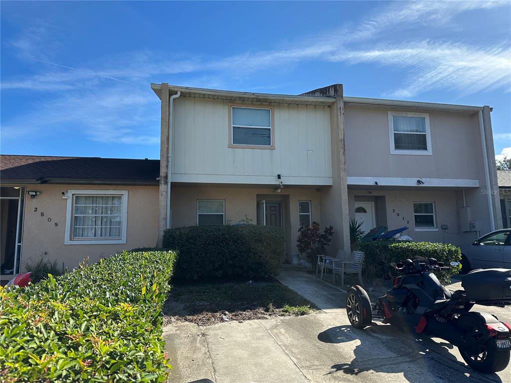 A two-story townhouse exterior features a beige facade, a hedge, and a parked three-wheeled motorcycle — 2513 RIO PINAR LAKES BOULEVARD, ORLANDO, FL