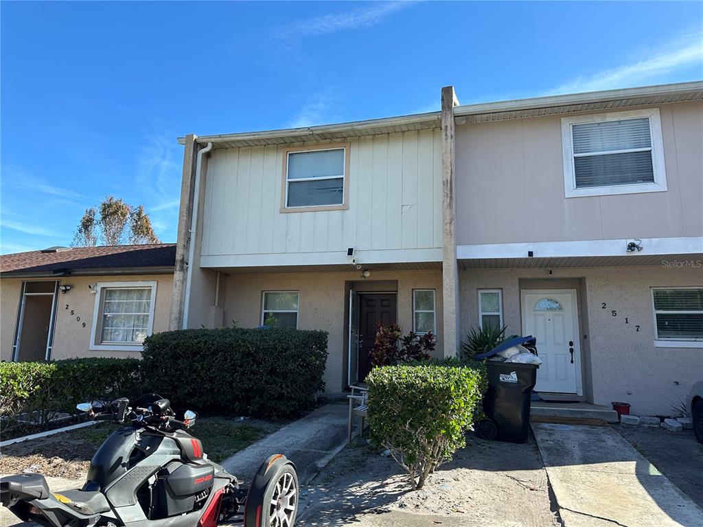 A two-story townhouse exterior features a concrete driveway, a small bush, and a parked motorcycle — 2513 RIO PINAR LAKES BOULEVARD, ORLANDO, FL