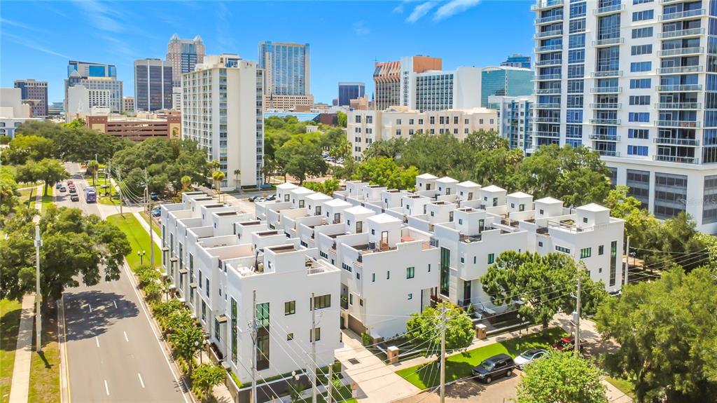 An aerial view shows a complex of modern white townhouses situated near a city skyline — 465 E SOUTH STREET UNIT 6, ORLANDO, FL