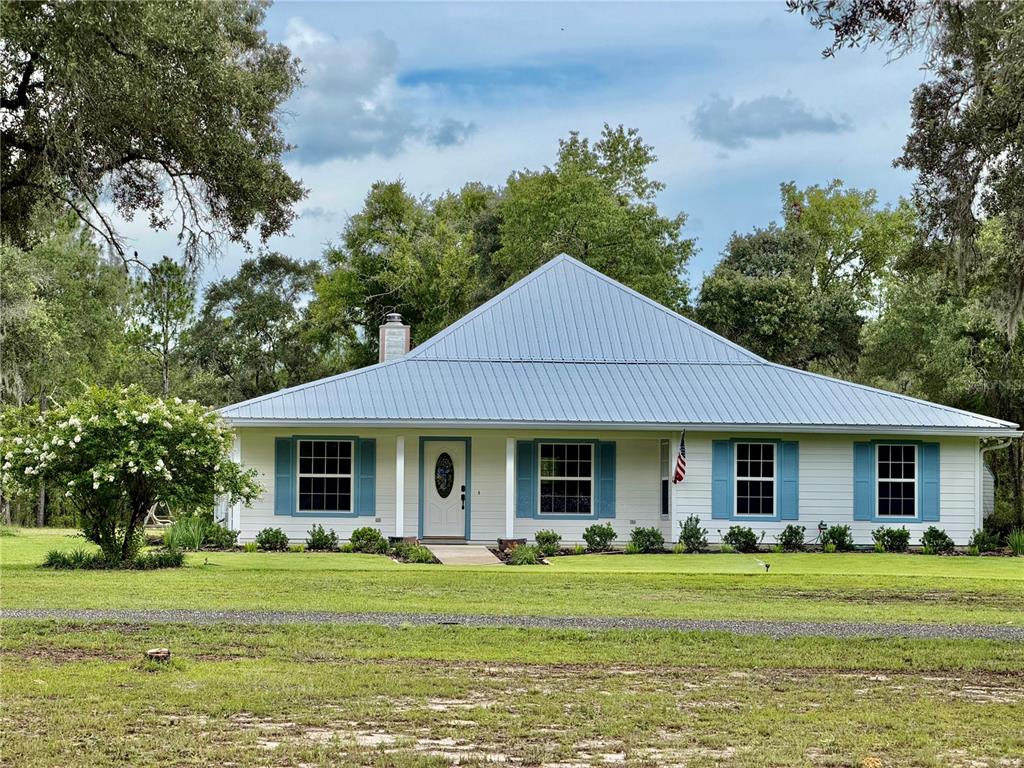 A single-story house with a metal roof, light siding, and blue shutters sits on a lawn — 14190 NE 75TH STREET, BRONSON, FL