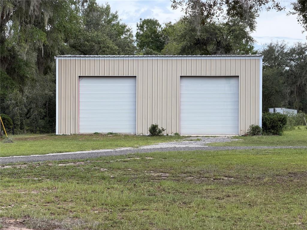A detached metal garage with two roll-up doors sits on a grassy lot — 14190 NE 75TH STREET, BRONSON, FL
