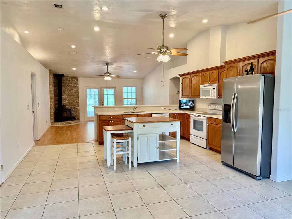 An open-concept kitchen features wood cabinets, a central island, and a stone fireplace nearby — 14190 NE 75TH STREET, BRONSON, FL