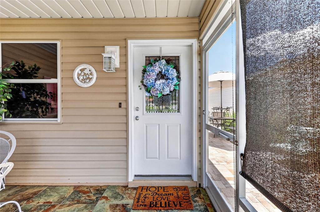A white front door with a floral wreath sits on a porch with tiled flooring — 356 KATHERINE PLACE, THE VILLAGES, FL