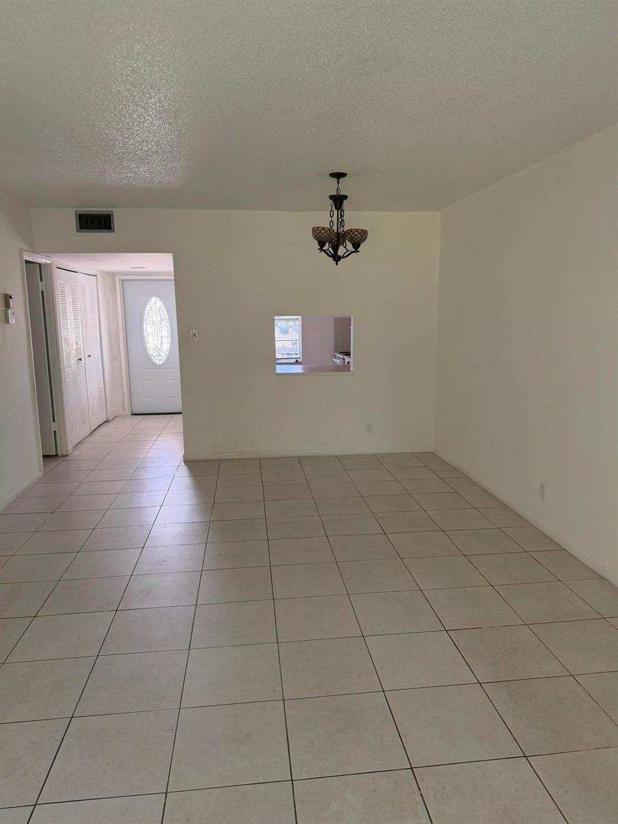 An empty room with beige tile flooring, a chandelier, and a pass-through window — 7205 W Atlantic Boulevard, Margate FL 33063, MARGATE, FL