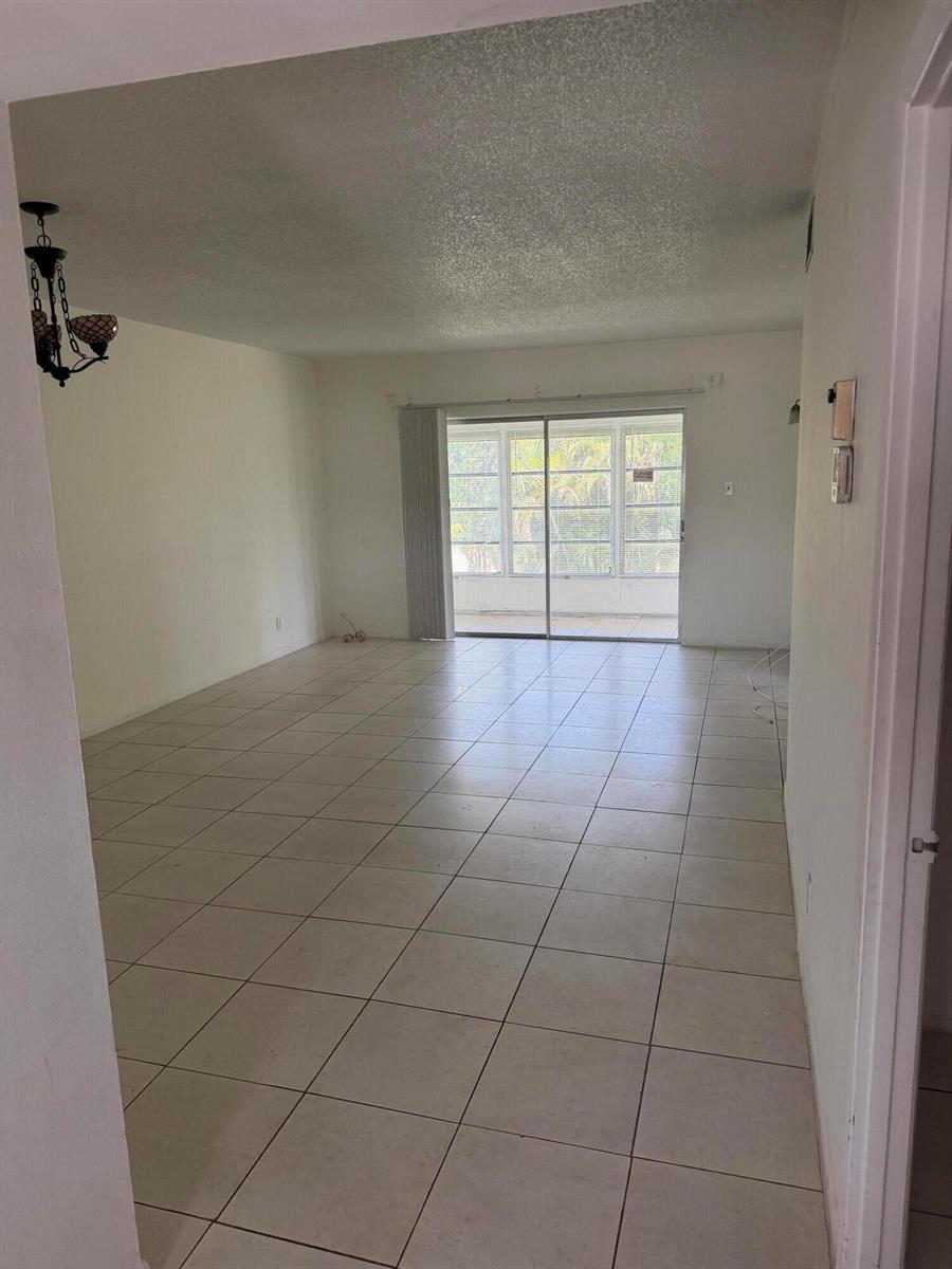 An empty living room with light-colored tile flooring and a sliding glass door to a patio — 7205 W Atlantic Boulevard, Margate FL 33063, MARGATE, FL
