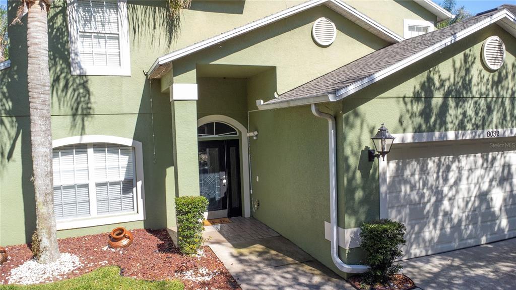 The exterior of a two-story green house features a front entrance and an attached garage — 8032 ACADIA ESTATES COURT, KISSIMMEE, FL
