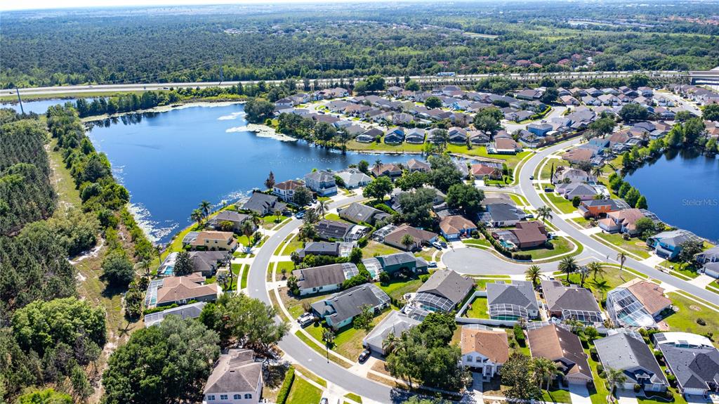 An aerial view shows a suburban neighborhood with houses surrounding a large lake — 8032 ACADIA ESTATES COURT, KISSIMMEE, FL