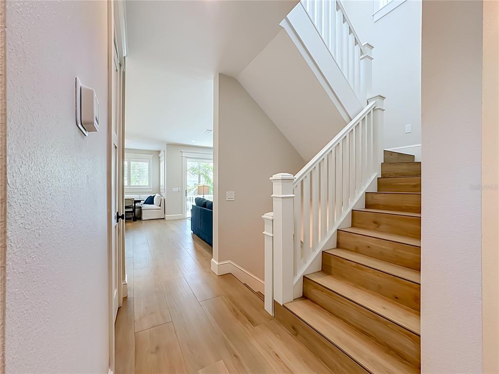 A hallway with light wood flooring leads to a living area beside a wooden staircase — 2918 GULF DRIVE, BRADENTON BEACH, FL