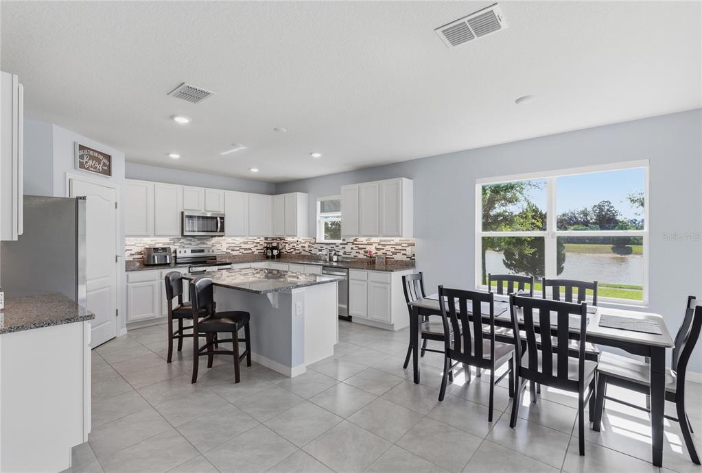 A kitchen with white cabinets, granite countertops, a center island, and an adjacent dining area — 2771 SUNNYVALE STREET, ST CLOUD, FL