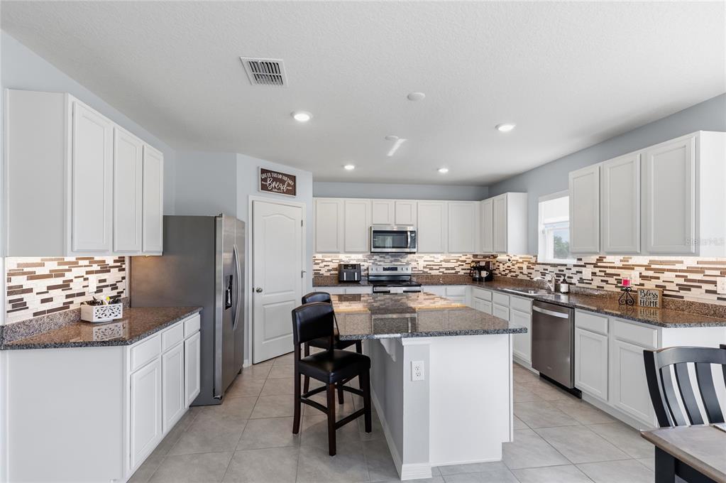 A kitchen features white cabinets, granite countertops, a center island, and stainless steel appliances — 2771 SUNNYVALE STREET, ST CLOUD, FL