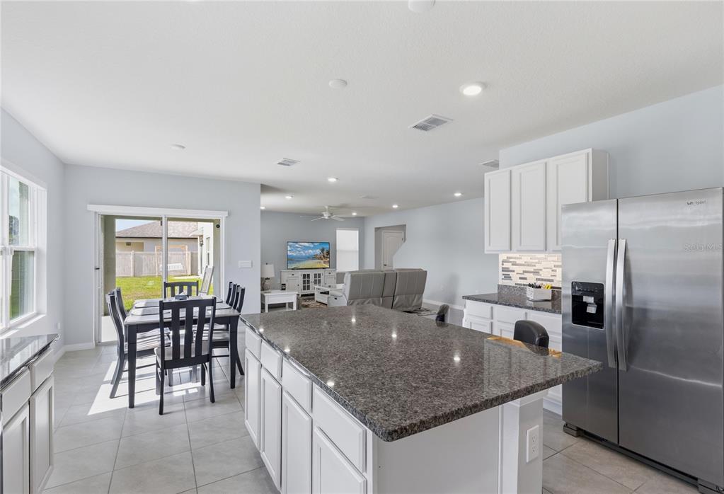 A kitchen with a granite island and white cabinets overlooks a dining area and living room — 2771 SUNNYVALE STREET, ST CLOUD, FL