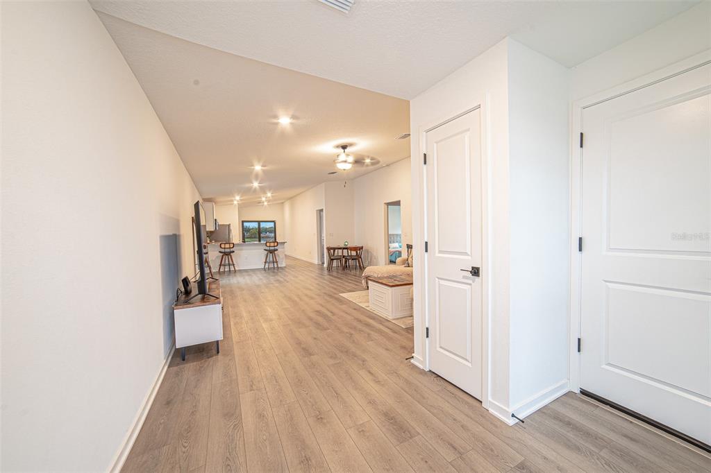 An open-concept living area features light wood-look flooring, a white door, and a kitchen beyond — 1375 AHOY AVENUE, TAMPA, FL