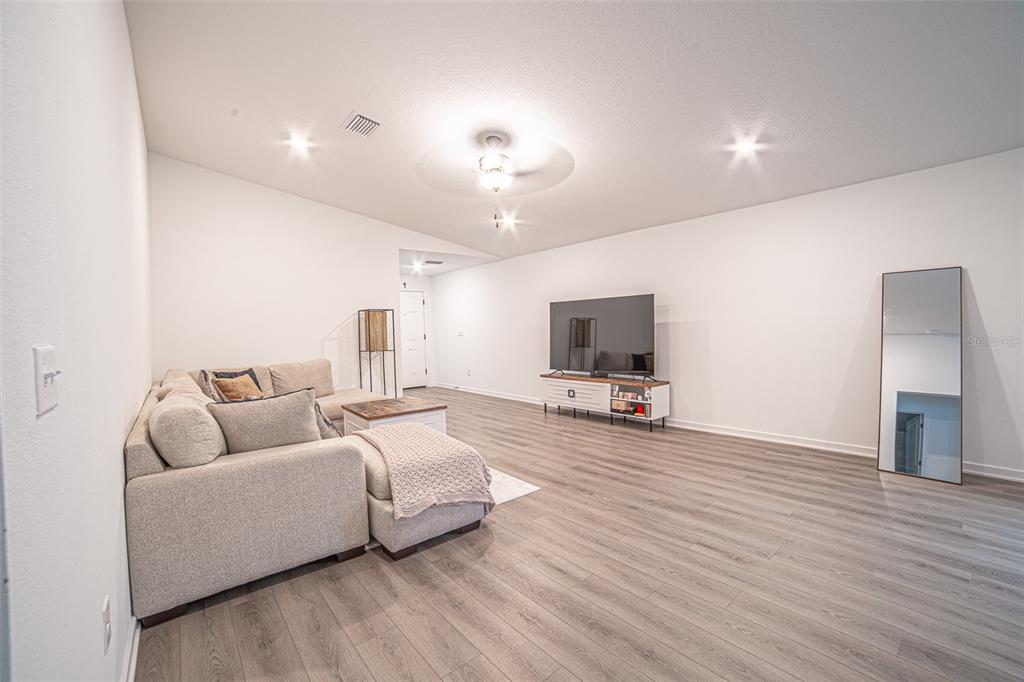 A living room features light wood-look flooring, a sectional sofa, a television, and a mirror — 1375 AHOY AVENUE, TAMPA, FL