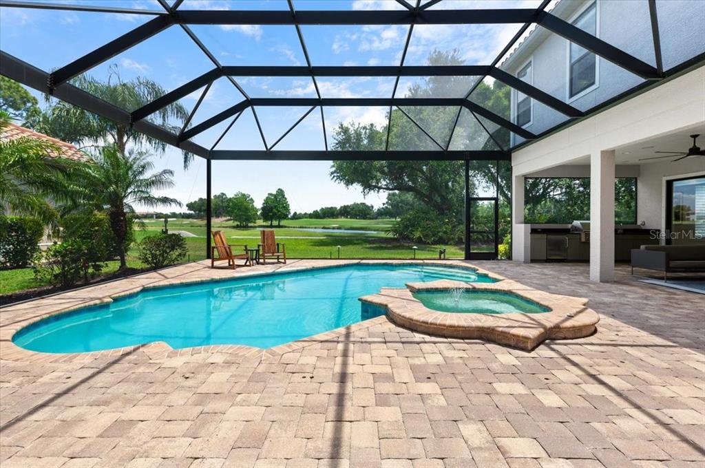 A screened-in patio features a swimming pool, a raised spa, and a view of a golf course — 7527 GREYSTONE STREET, LAKEWOOD RANCH, FL